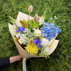 Bouquet of flowers held against a green hedge