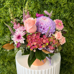 Colorful flower arrangement on a white pedestal against a green hedge background