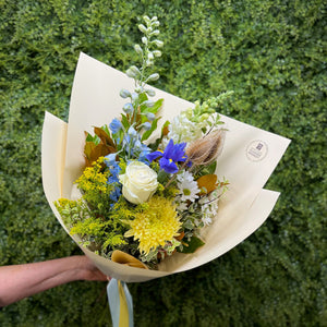 Bouquet of yellow, white and blue flowers held against a green background