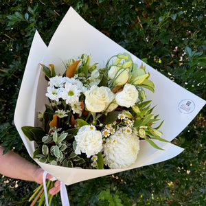Bouquet of white flowers with greenery held against a green leafy background