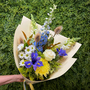 Bouquet of blue, white and yellow flowers held against a green hedge