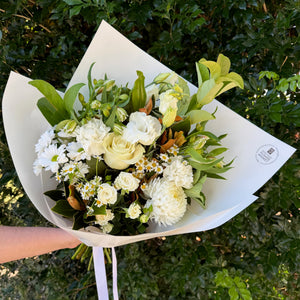 Bouquet of flowers wrapped in white paper held against a green leafy background