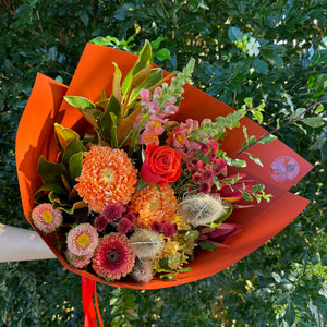 Bouquet of flowers in an orange paper wrap against a green leafy background