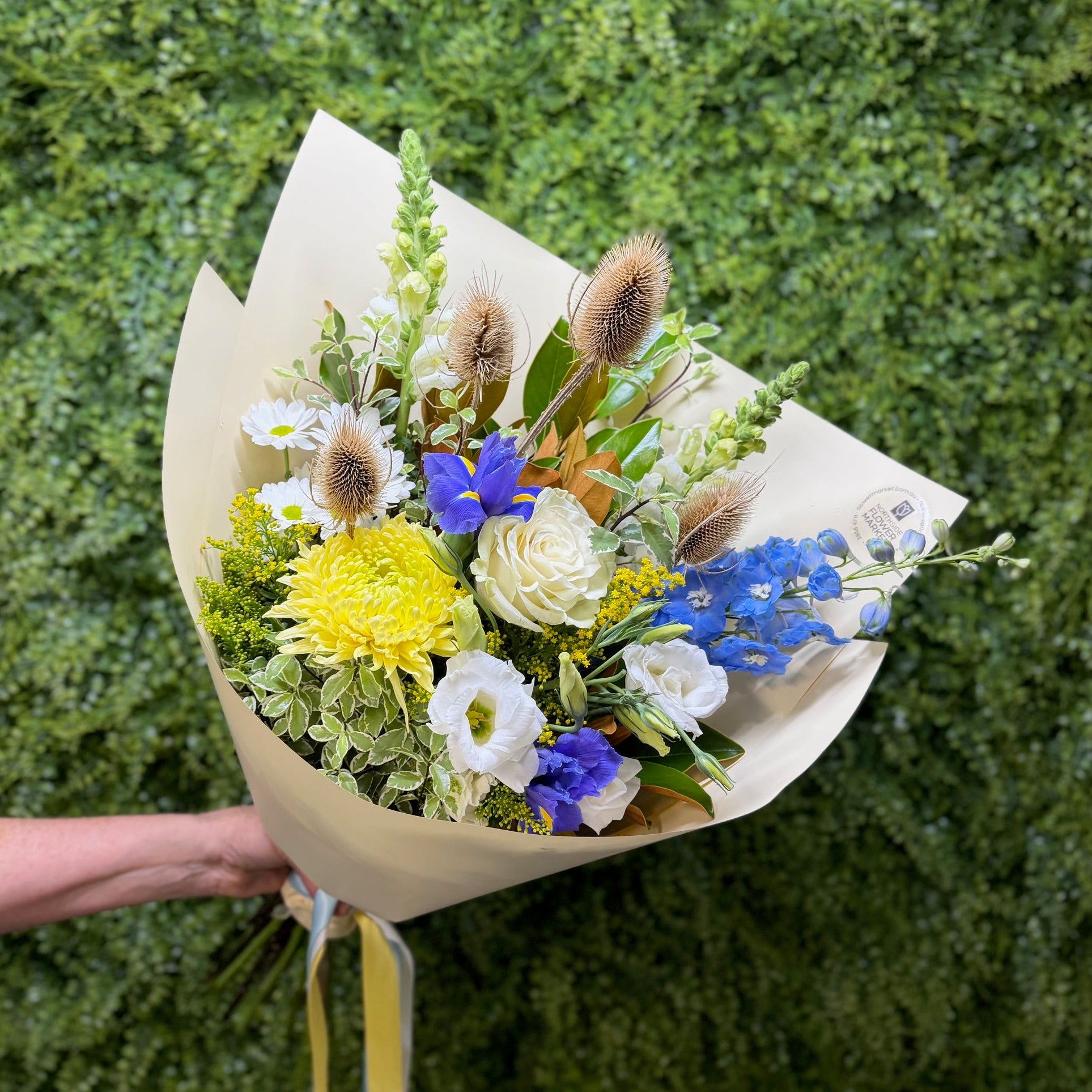 Bouquet of blue, white and yellow flowers held against a green textured background