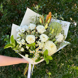 Bouquet of white flowers held against a green bush background