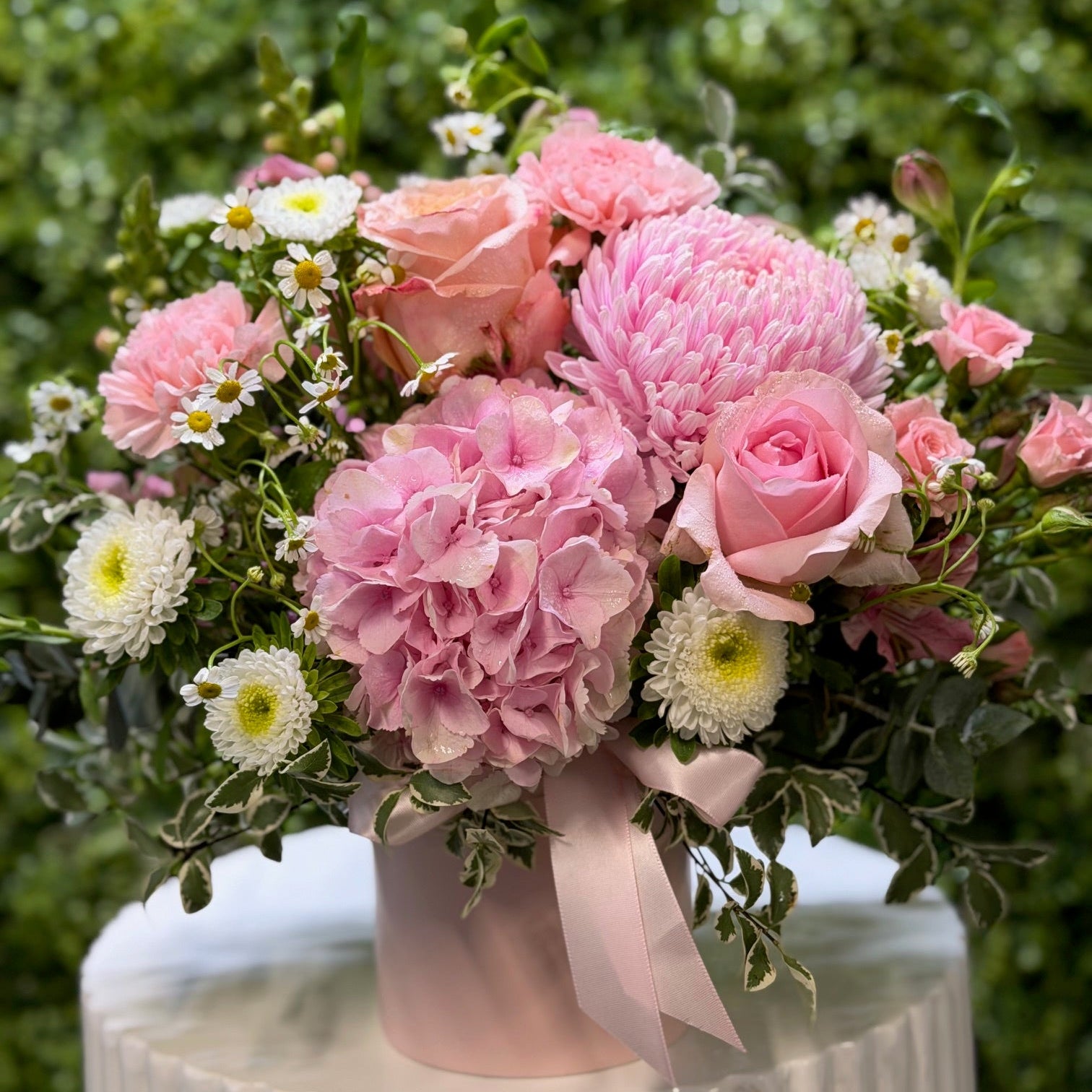 Bouquet of pink flowers with greenery on a white pedestal against a blurred green background