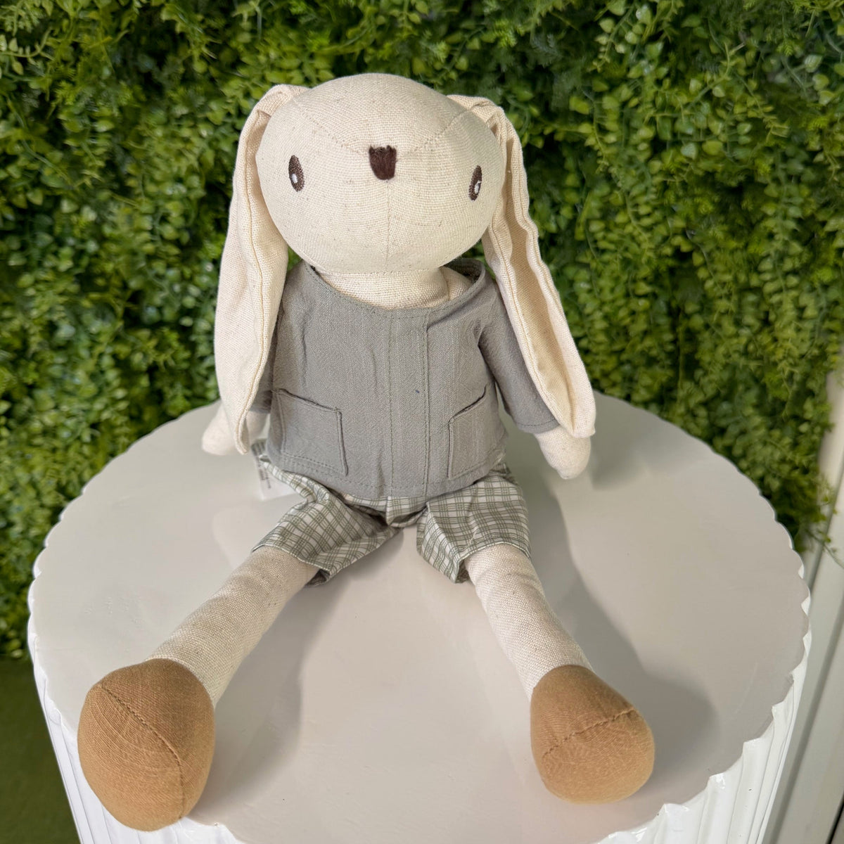 Toy figure of a rabbit with a gray outfit sitting on a white surface with a green background