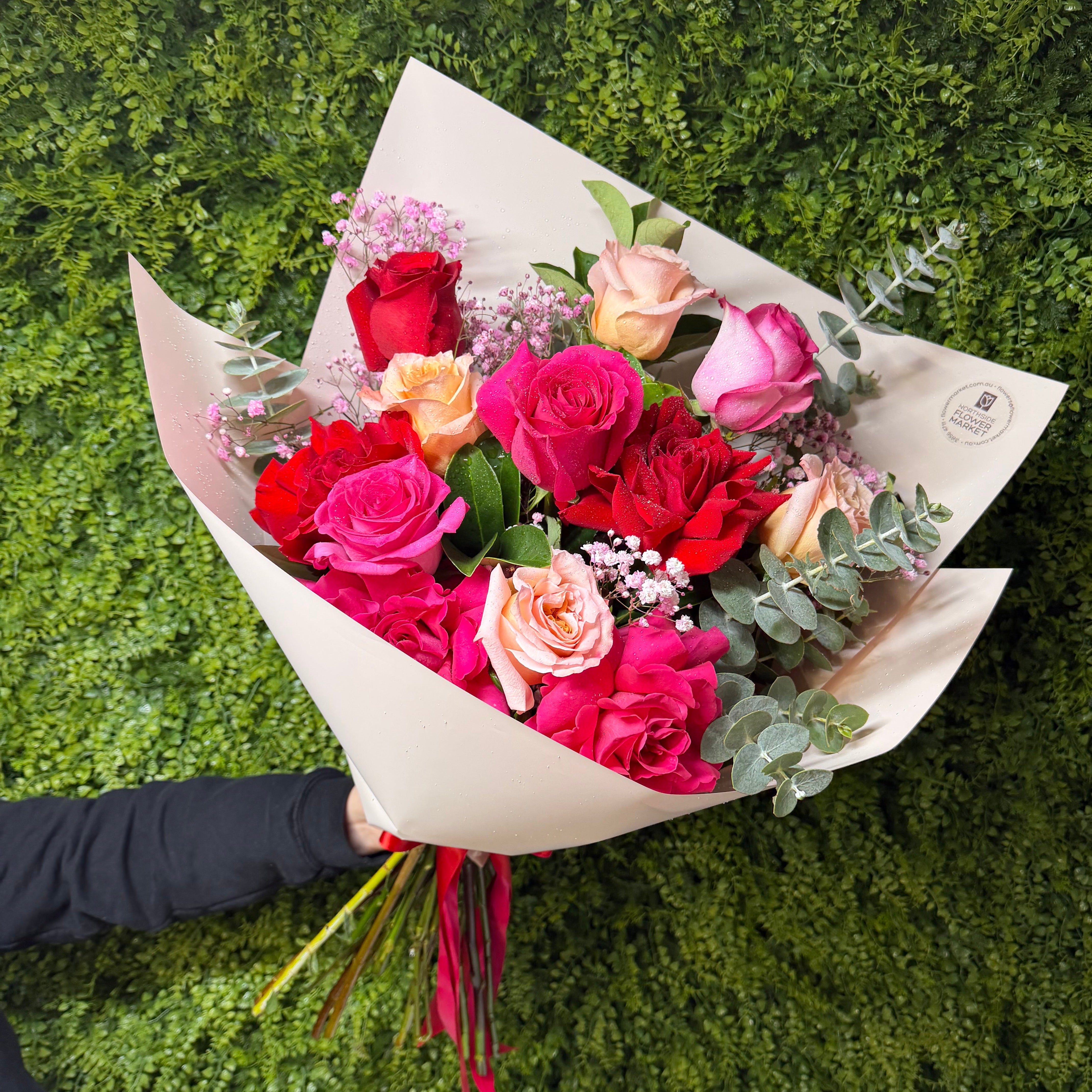 Bouquet of red, pink, and peach roses held against a green background