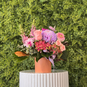 Floral arrangement in a pink vase on a white pedestal against a green hedge background