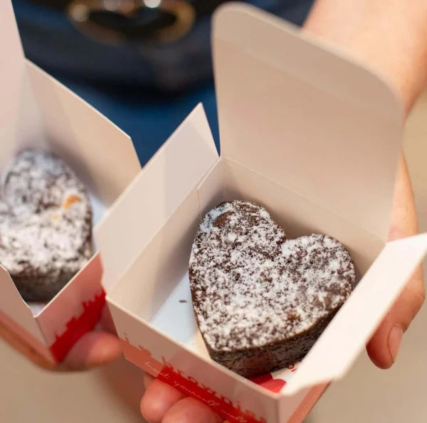 Heart-shaped gluten free chocolate brownie in a takeout box held by a person.