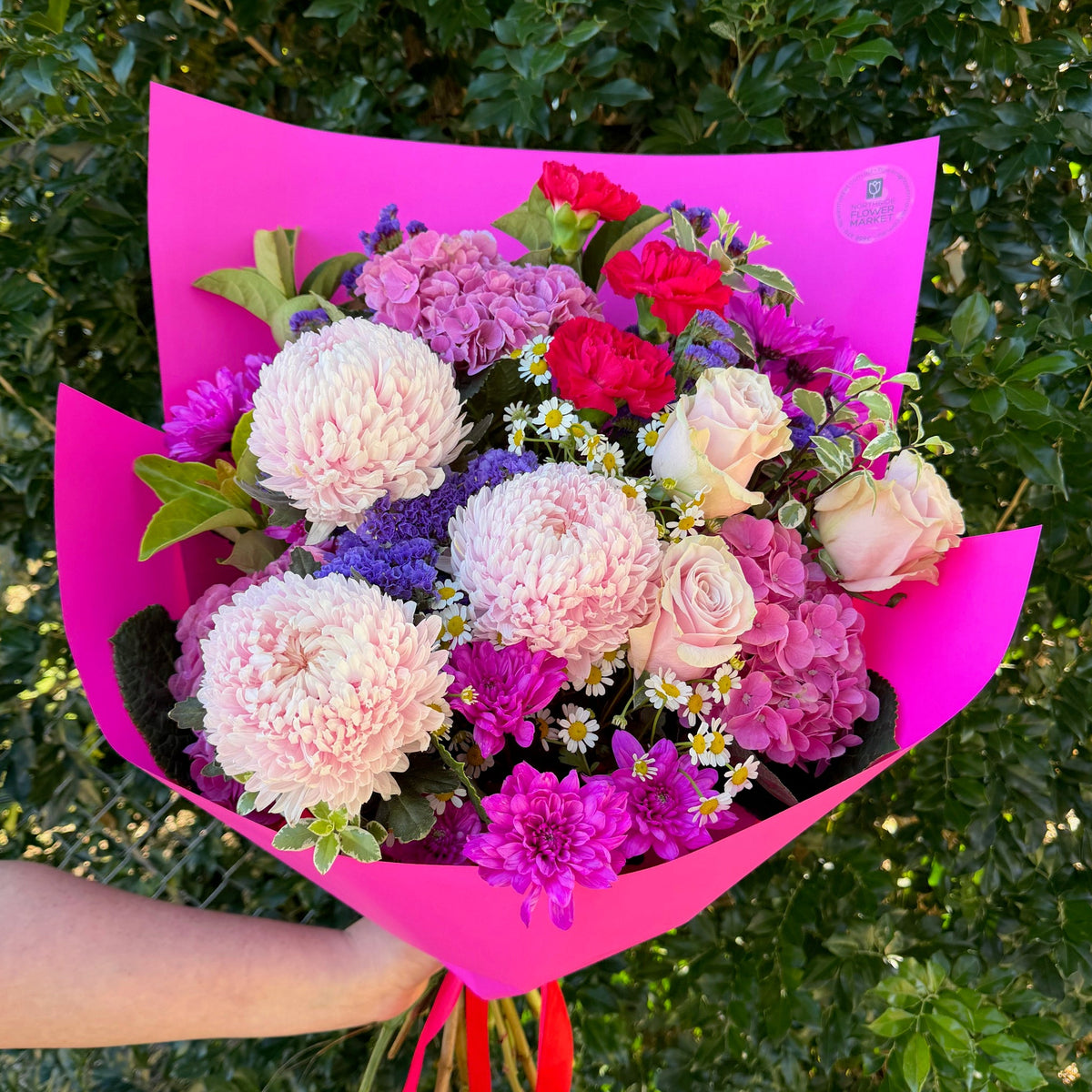 Bouquet of flowers wrapped in pink paper held by a person against a green leafy background