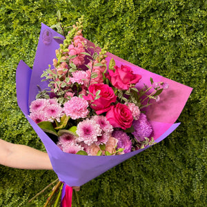 Bouquet of pink and purple flowers wrapped in purple paper against a green grass background