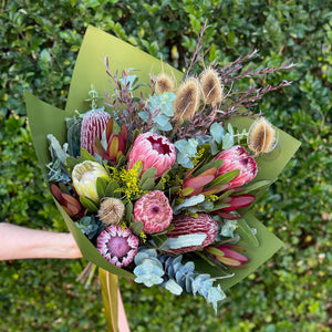 Bouquet of native flowers including proteas, banksias and leucadendrons held against a green bush background