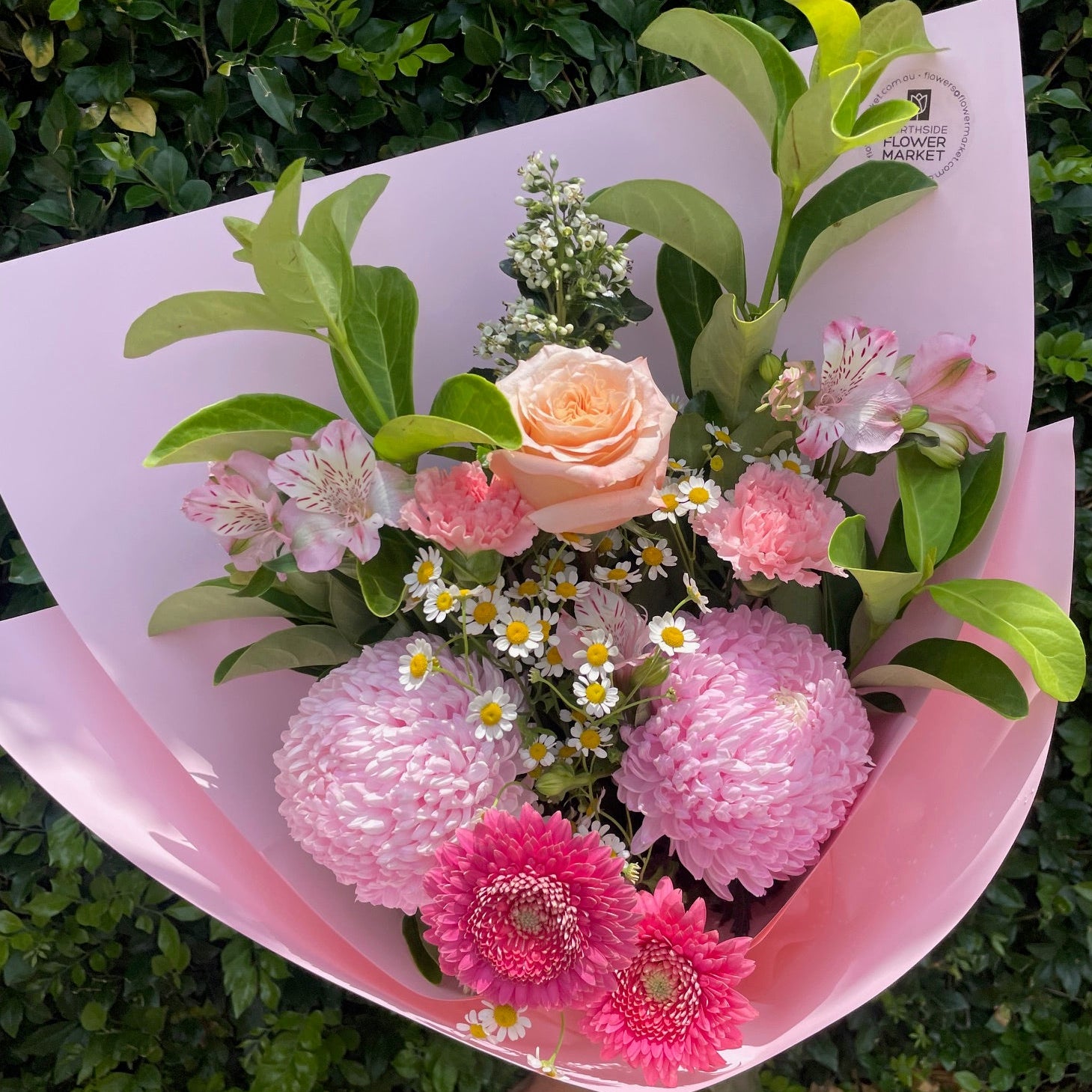 Bouquet of flowers wrapped in pink paper against a green leafy background