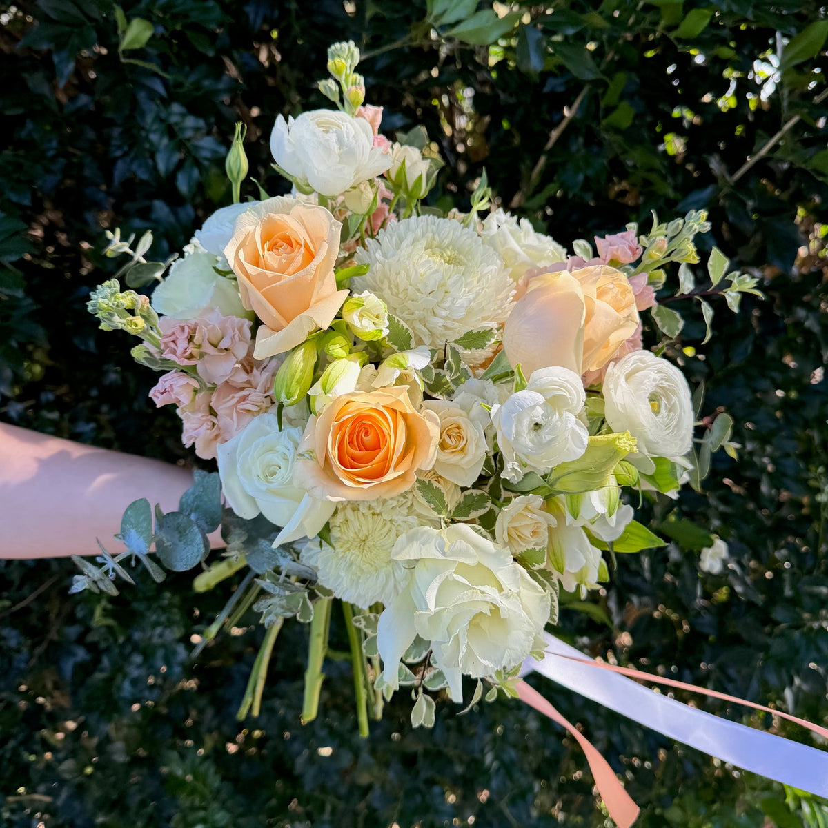 Wedding bouquet of flowers held by a hand with a green leafy background