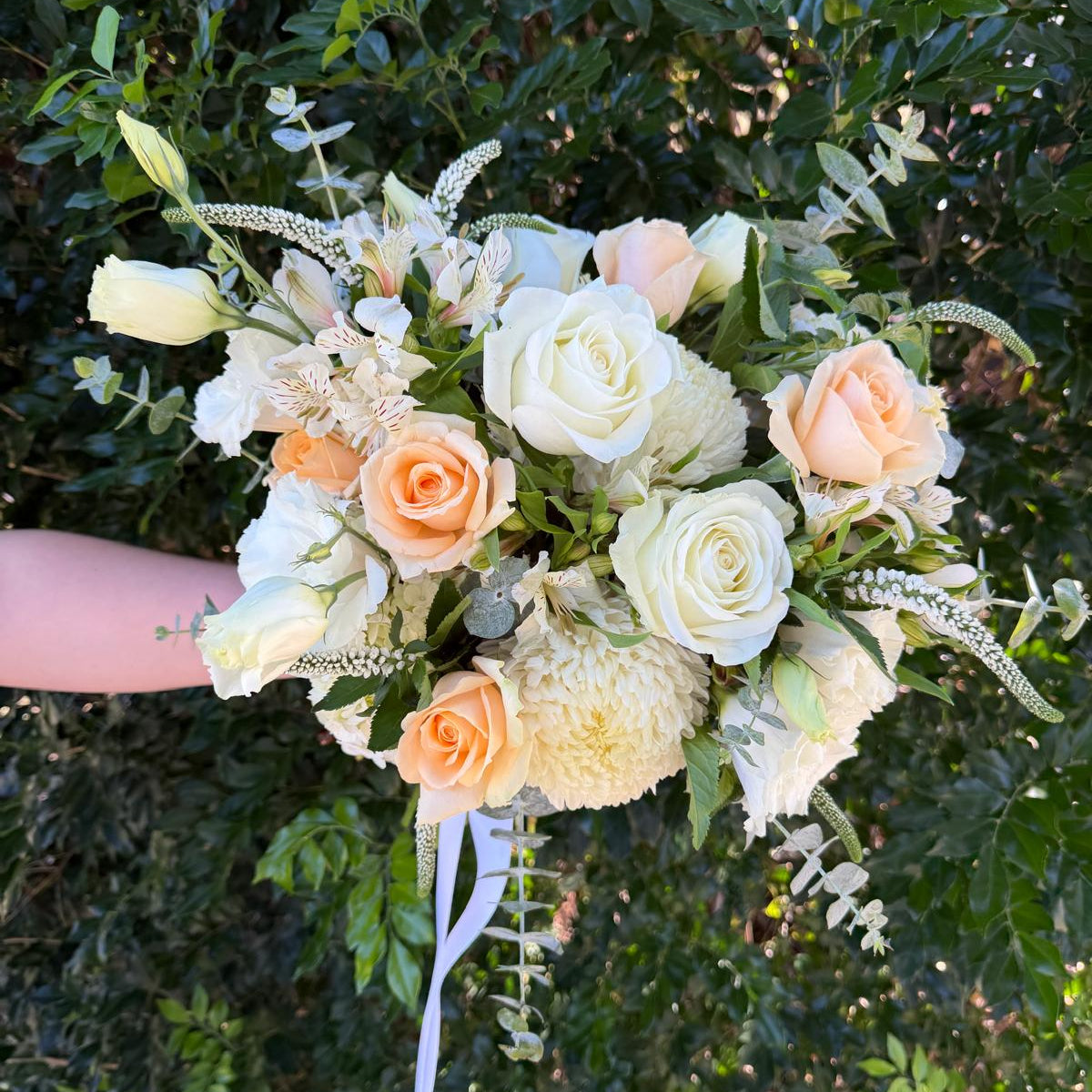 Wedding bouquet of white and peach roses held against a green leafy background