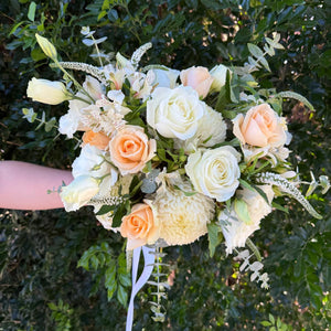 Wedding bouquet of white and peach roses held against a green leafy background