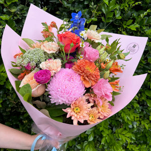 Bouquet of flowers wrapped in pink paper held against a green leafy background