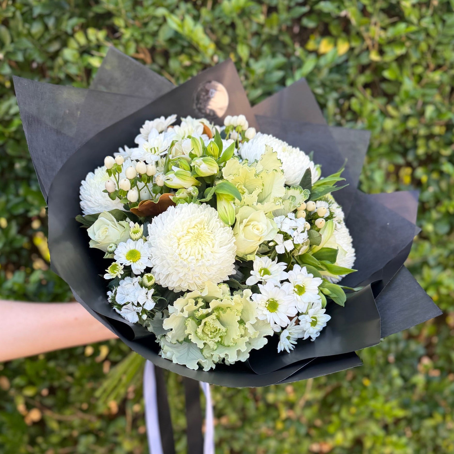 Bouquet of white and green flowers held by a person against a green bush background
