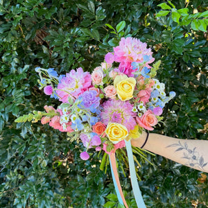 Colorful floral wedding bouquet held by a person against a green leafy background